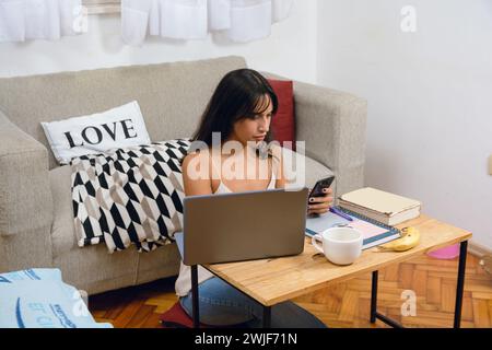 Jeune femme entrepreneure brune Latina à la maison assise occupée à travailler avec son ordinateur portable examinant l'agenda de planification téléphonique et les rendez-vous avec son client Banque D'Images