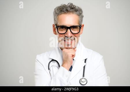 Cette image montre un médecin expérimenté avec des lunettes, posant réfléchi avec son menton posé sur sa main, signalant qu'il est prêt à s'engager et à écouter les préoccupations des patients. Banque D'Images