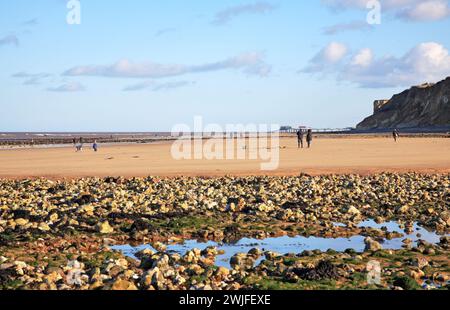 Une vue vers l'est le long de la plage avec des silex, du sable et des gens par un bel après-midi d'hiver à West Runton, Norfolk, Angleterre, Royaume-Uni. Banque D'Images