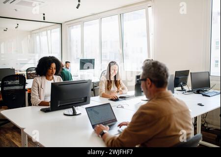Une équipe de professionnels travaille avec diligence dans un espace de bureau lumineux et ouvert. L'environnement moderne et collaboratif met l'accent sur un mélange de concentration et d'interaction entre divers collègues Banque D'Images