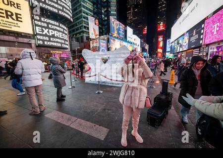 Les touristes assistent à la sculpture sur glace « frappée » de Lovie Pignata, lauréate du Winter Ice sculpture Show sur Governor’s Island, à Times Square à New York le mercredi 14 février 2024, jour de la Saint-Valentin. Les deux moufles sculptées dans la glace formant un cœur ont été redimensionnées par le studio Okamoto et seront exposées à Duffy Square jusqu’à ce qu’elle « s’autodétruise » en fondant. (© Richard B. Levine) Banque D'Images