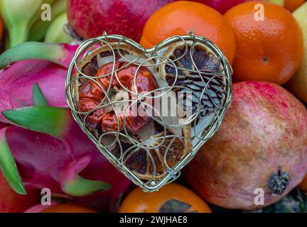 Le cas de maille en forme de coeur doré est rempli de fruits séchés sur une variété de fruits assortis. Concept d'amour coloré, espace de copie, mise au point sélective. Banque D'Images