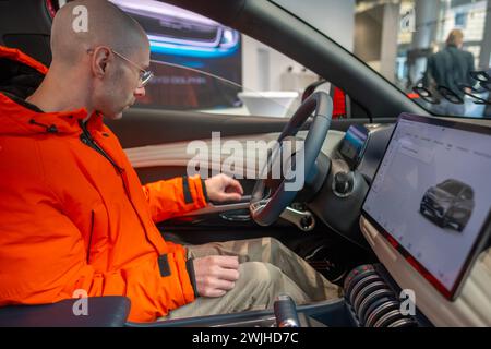 Jeune homme examine, choisit la nouvelle voiture rouge BYD ATTO 3, derrière le volant du véhicule électrique fabricant chinois BYD, essai routier, industr automobile Banque D'Images