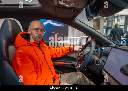 Jeune homme examine, choisit la nouvelle voiture rouge BYD ATTO 3, derrière le volant du véhicule électrique fabricant chinois BYD, essai routier, industr automobile Banque D'Images