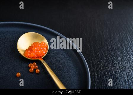 Caviar rouge dans la cuillère dorée sur fond d'ardoise noire gros plan Banque D'Images