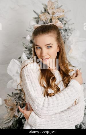 Portrait de jolie jeune femme avec les bras pliés sur sa poitrine et avec arbre de Noël sur fond Banque D'Images