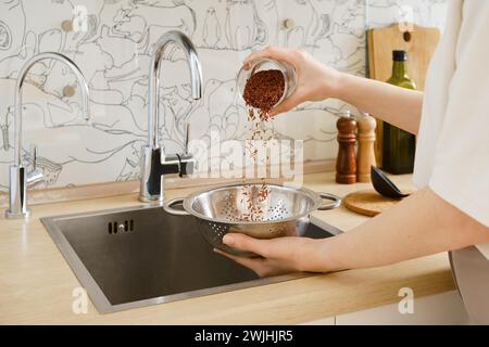 Femme méconnaissable verse le riz d'un verre dans une passoire pour le rincer sous l'eau courante Banque D'Images