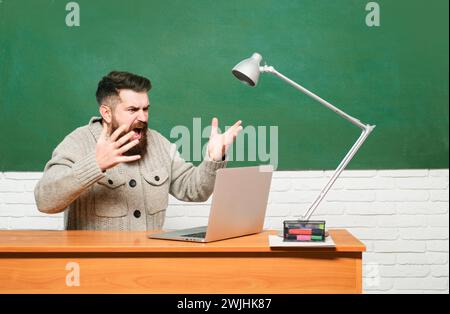 Tuteur. Jeune enseignant près du tableau noir dans la salle de classe de l'école. Journée des enseignants. Professeur barbu en classe d'éducation près de Blackboard. Banque D'Images