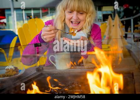 Femme appréciant le café et mangeant le gâteau de carotte à l'extérieur par le feu chaud en hiver Banque D'Images