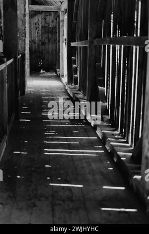 À l'intérieur de la grange avec la lumière du soleil brisant à travers le mur de bois jetant des ombres légères sur le sol. Banque D'Images