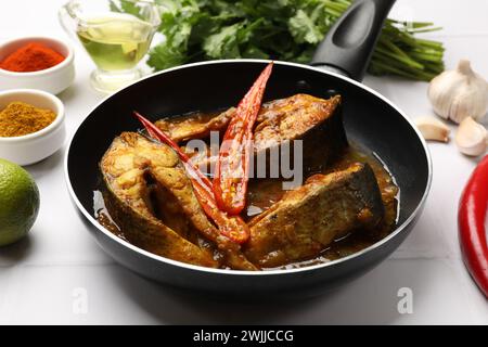 Délicieux curry de poisson dans une poêle à frire et ingrédients sur une table carrelée blanche, gros plan. Cuisine indienne Banque D'Images