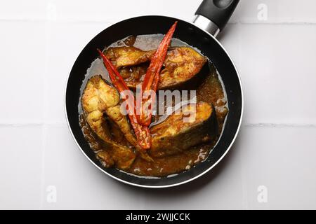 Délicieux curry de poisson dans une poêle à frire sur une table carrelée blanche, vue de dessus. Cuisine indienne Banque D'Images