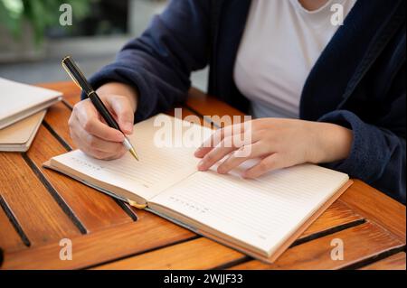 Photo recadrée d'une femme en vêtements décontractés écrivant ses idées dans un livre alors qu'elle était assise dans un café. tenir un journal, noter, faire une liste Banque D'Images