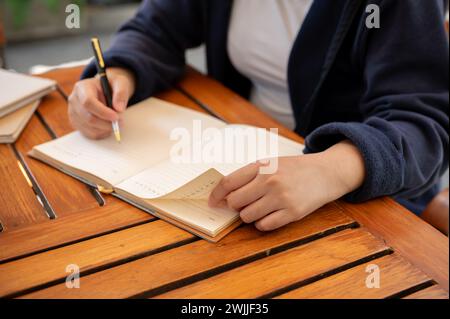 Photo recadrée d'une femme en vêtements décontractés écrivant ses idées dans un livre alors qu'elle était assise dans un café. tenir un journal, noter, faire une liste Banque D'Images