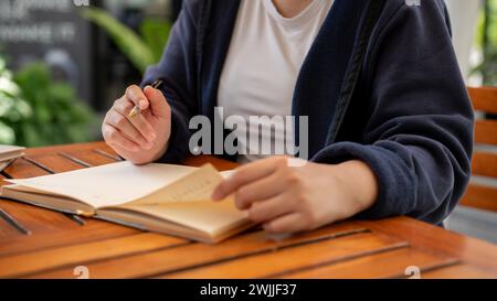Photo recadrée d'une femme en vêtements décontractés écrivant ses idées dans un livre alors qu'elle était assise dans un café. tenir un journal, noter, faire une liste Banque D'Images