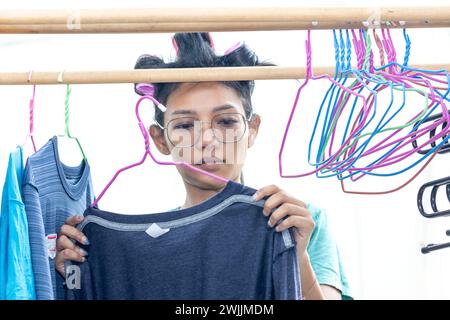 Une jeune femme avec des bigoudis dans les cheveux accroche du linge mouillé sur des cintres Banque D'Images