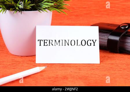 TERMINOLOGIE texte écrit sur une carte de visite à côté d'un porte-carte de visite, une fleur verte et un crayon sur un fond orange Banque D'Images