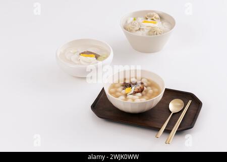 Sur une table blanche, trois bols de soupe de gâteau de riz sont placés avec du kimchi Banque D'Images