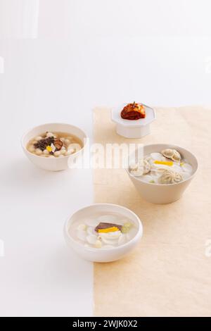 Trois bols de soupe de gâteau de riz et de kimchi sont placés sur une table blanche recouverte de papier coréen Banque D'Images