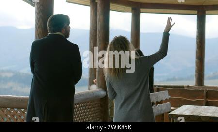 La famille avec enfants visite une nouvelle propriété potentielle avec un agent immobilier. Agent immobilier féminin avec tablette numérique montre chalet en bois dans les montagnes aux clients. Concept de location ou d'achat. Banque D'Images