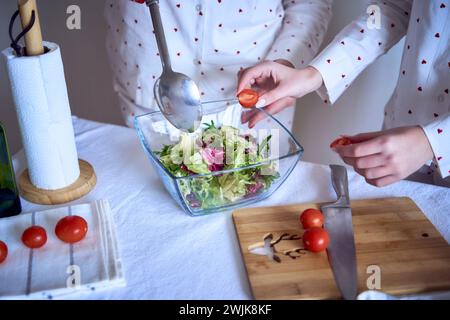 adolescente et sa mère en pyjama cuisinent et mangent une salade verte fraîche et de tomates ensemble Banque D'Images