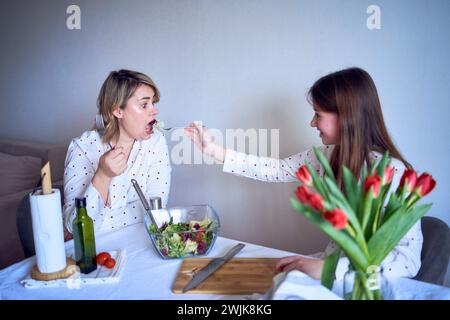 adolescente et sa mère en pyjama cuisinent et mangent une salade verte fraîche et de tomates ensemble Banque D'Images