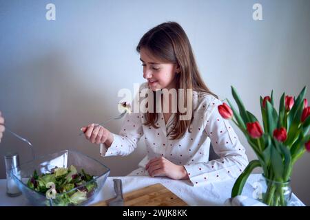 adolescente et sa mère en pyjama cuisinent et mangent une salade verte fraîche et de tomates ensemble Banque D'Images