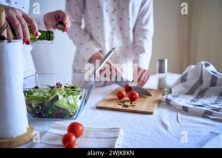 adolescente et sa mère en pyjama cuisinent et mangent une salade verte fraîche et de tomates ensemble Banque D'Images