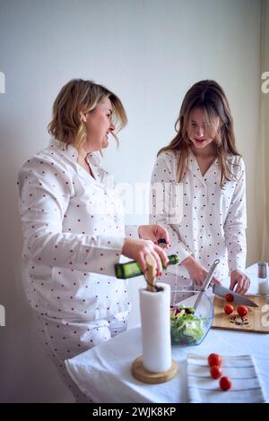 adolescente et sa mère en pyjama cuisinent et mangent une salade verte fraîche et de tomates ensemble Banque D'Images