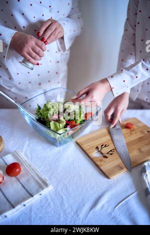 adolescente et sa mère en pyjama cuisinent et mangent une salade verte fraîche et de tomates ensemble Banque D'Images