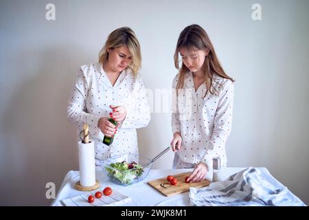 adolescente et sa mère en pyjama cuisinent et mangent une salade verte fraîche et de tomates ensemble Banque D'Images