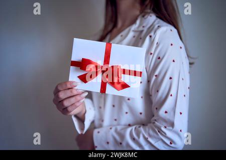 un certificat cadeau entre les mains d'une adolescente portant un pyjama blanc avec des coeurs rouges Banque D'Images