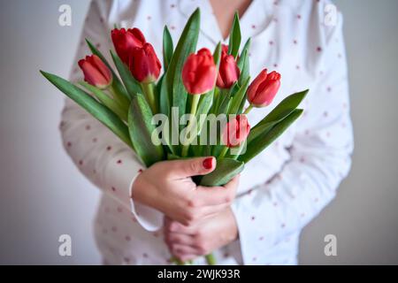 un portrait d'une belle femme de taille moyenne en pyjama avec un bouquet de tulipes rouges dans un style minimaliste Banque D'Images