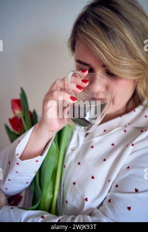 un portrait d'une belle femme de taille moyenne en pyjama avec un bouquet de tulipes rouges dans un style minimaliste Banque D'Images