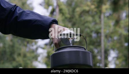 Bouilloire touristique se tient sur la cuisinière à gaz portable de camping. Un voyageur masculin allume un brûleur à gaz. Groupe de copains de randonnée s'est arrêté pour se reposer après trek dans les montagnes. Concept de découverte de la nature et de loisirs actifs. Banque D'Images