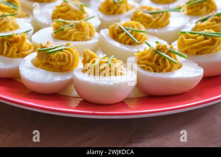 Gros plan d'œufs farcis avec deux brins de ciboulette sur une assiette blanche sur une table en bois. Banque D'Images