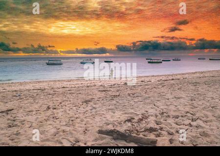 Un touriste marchant sur la plage de sable de Malindi Beach au lever du soleil avec des bateaux de pêche en arrière-plan à Malindi, Kenya Banque D'Images