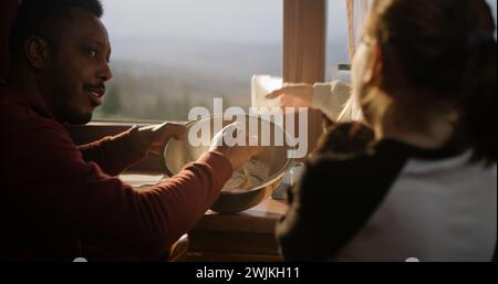 Couple multiethnique cuisiner ensemble, parler avec la fille dans la cuisine de la maison de vacances. Jeune fille avec chat sur les mains se tient près des parents. Voyageurs famille arrêté pour se reposer dans le chalet pendant les vacances. Gros plan. Banque D'Images