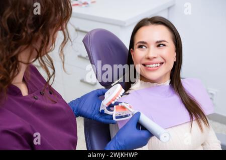 Professionnel dentaire explique à la patiente comment se brosser les dents correctement en clinique. Les dentistes utilisent le modèle dentaire de mâchoire humaine pour plus de clarté Banque D'Images