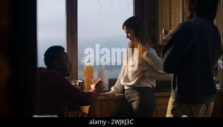 Couple touristique multiethnique cuisiner ensemble dans la cuisine de la maison de vacances. Adolescent afro-américain vient à ses parents et regarde dans le réfrigérateur. Famille voyageur arrêté pour se reposer dans un chalet en bois pendant les vacances. Banque D'Images