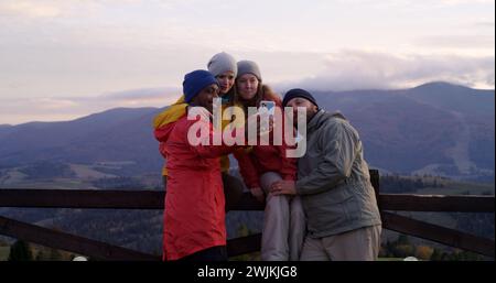 Les copains de randonnée se tiennent près d'une clôture en bois et regardent le coucher du soleil. Groupe de divers touristes ou voyageurs apprécient le paysage des montagnes et la belle nature pendant le voyage. Passionnés d'activités de plein air. Ralenti. Banque D'Images