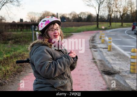 Heureuse femme blanche de 41 ans avec le syndrome de Down, debout sur une piste cyclable, Tienen, Belgique Banque D'Images