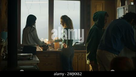 Deux femmes touristes cuisinent ensemble dans la maison de vacances, jeune fille avec le chat sur les mains se tient près d'eux. L'homme vient dans la cuisine et regarde dans le frigo. Voyageurs famille arrêté pour se reposer dans le chalet pendant les vacances. Banque D'Images