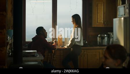 Couple touristique multiethnique cuisiner ensemble dans la cuisine de la maison de vacances. Adolescent afro-américain vient à ses parents et regarde dans le réfrigérateur. Famille voyageur arrêté pour se reposer dans un chalet en bois pendant les vacances. Banque D'Images