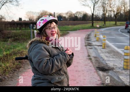 Heureuse femme blanche de 41 ans avec le syndrome de Down, debout sur une piste cyclable, Tienen, Belgique Banque D'Images