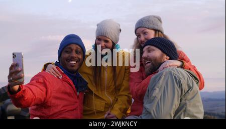 Les copains de randonnée se tiennent près d'une clôture en bois et regardent le coucher du soleil. Groupe de divers touristes ou voyageurs apprécient le paysage des montagnes et la belle nature pendant le voyage. Passionnés d'activités de plein air. Ralenti. Banque D'Images