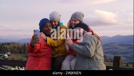 Les copains de randonnée se tiennent près d'une clôture en bois et regardent le coucher du soleil. Groupe de divers touristes ou voyageurs apprécient le paysage des montagnes et la belle nature pendant le voyage. Passionnés d'activités de plein air. Ralenti. Banque D'Images