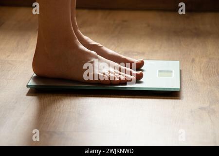 Les pieds de la femme se tiennent sur une balance de salle de bain à la maison sur le sol dans la lumière Banque D'Images