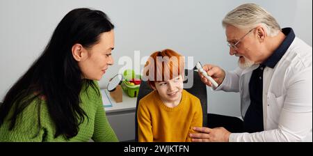 Mère avec enfant masculin audiologiste pédiatrique visitant pour le bilan auditif. Garçon roux ayant une otoscopie en audiologie Banque D'Images