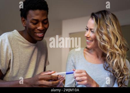 Couple heureux souriant tout en tenant le test de grossesse dans la chambre Banque D'Images
